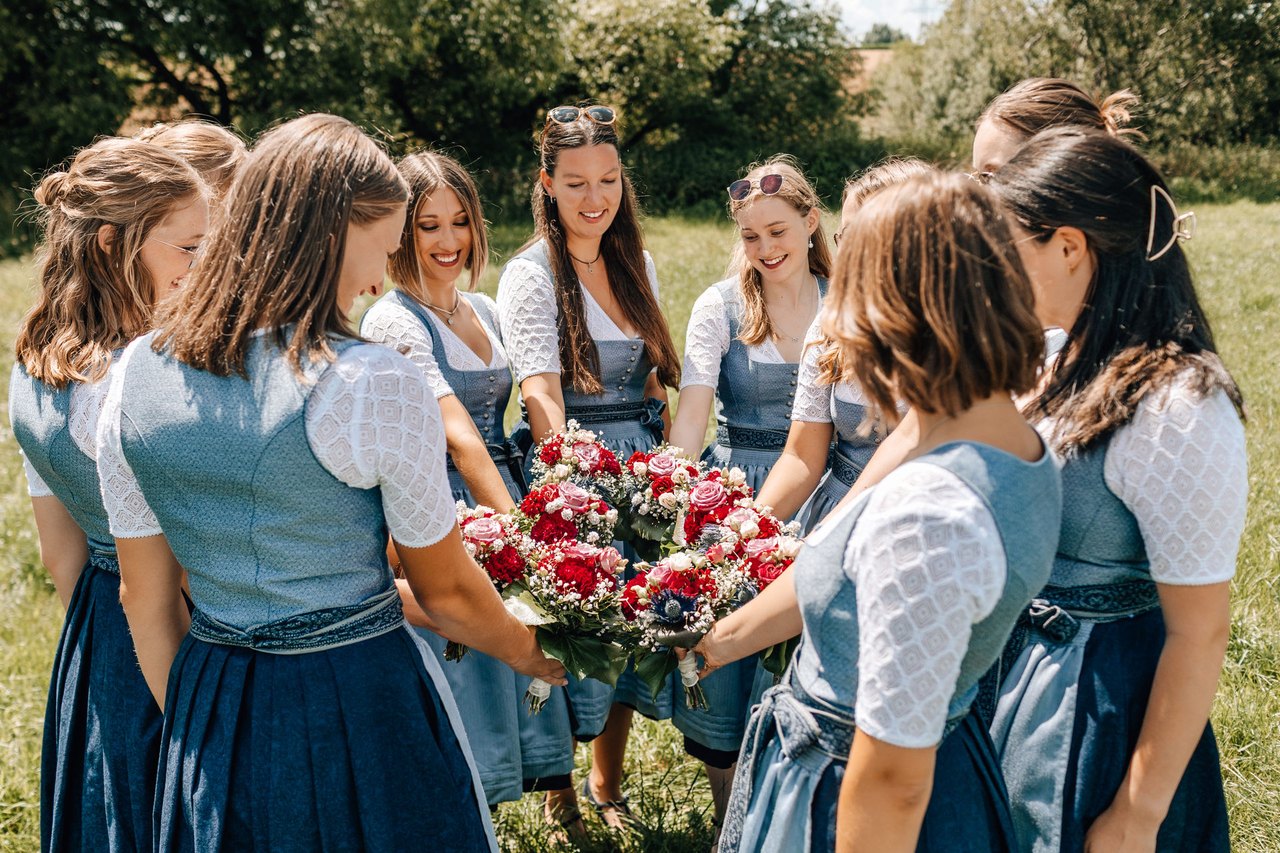 Festdamen stehen im Kreis und halten ihre Blumensträuße zusammen