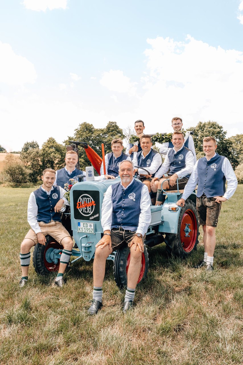 Die Vorstandschaft des Burschenvereins Gmoa Wörth in Tracht auf und neben einem hellblauen Eicher-Bulldog