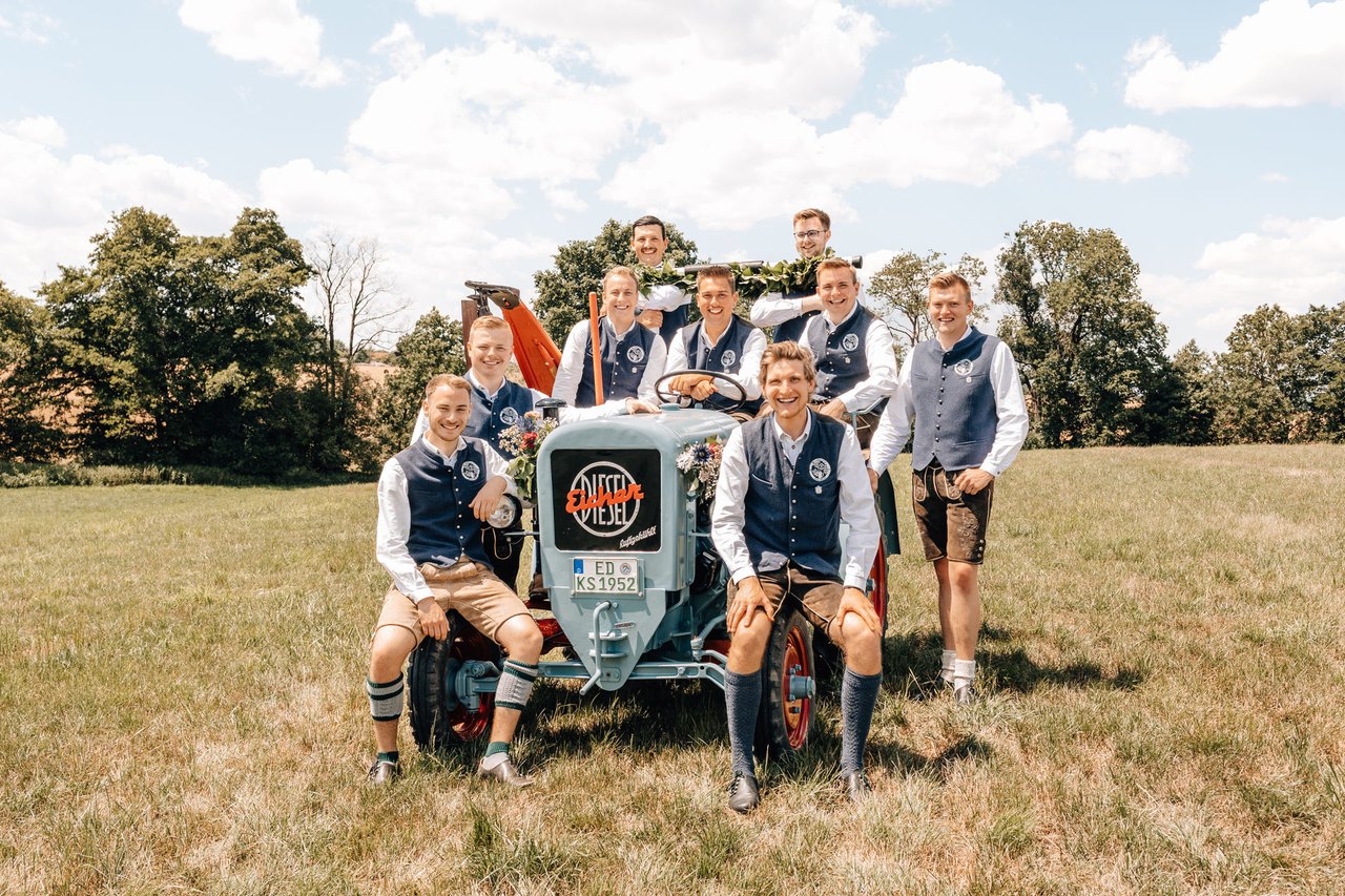 Gruppenbild der Vorstandschaft in Tracht rund um einen hellblauen Eicher-Bulldog auf der Wiese